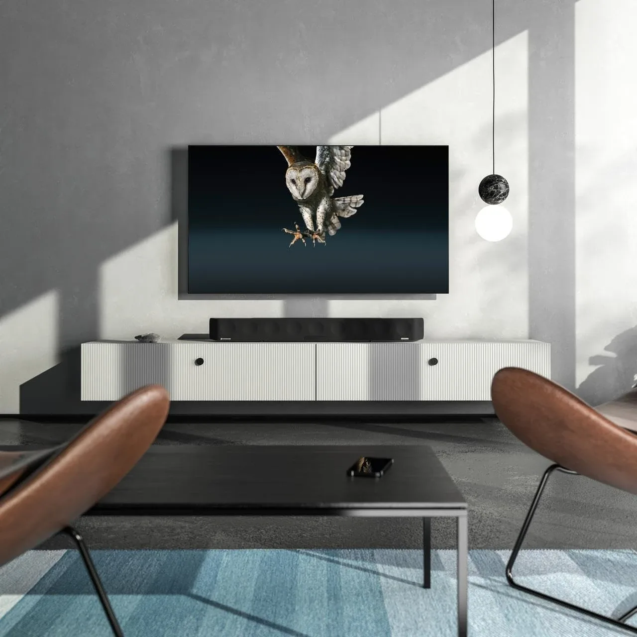 The AMBEO Soundbar Max on a low sideboard beneath a wall-mounted television in a bright living room
