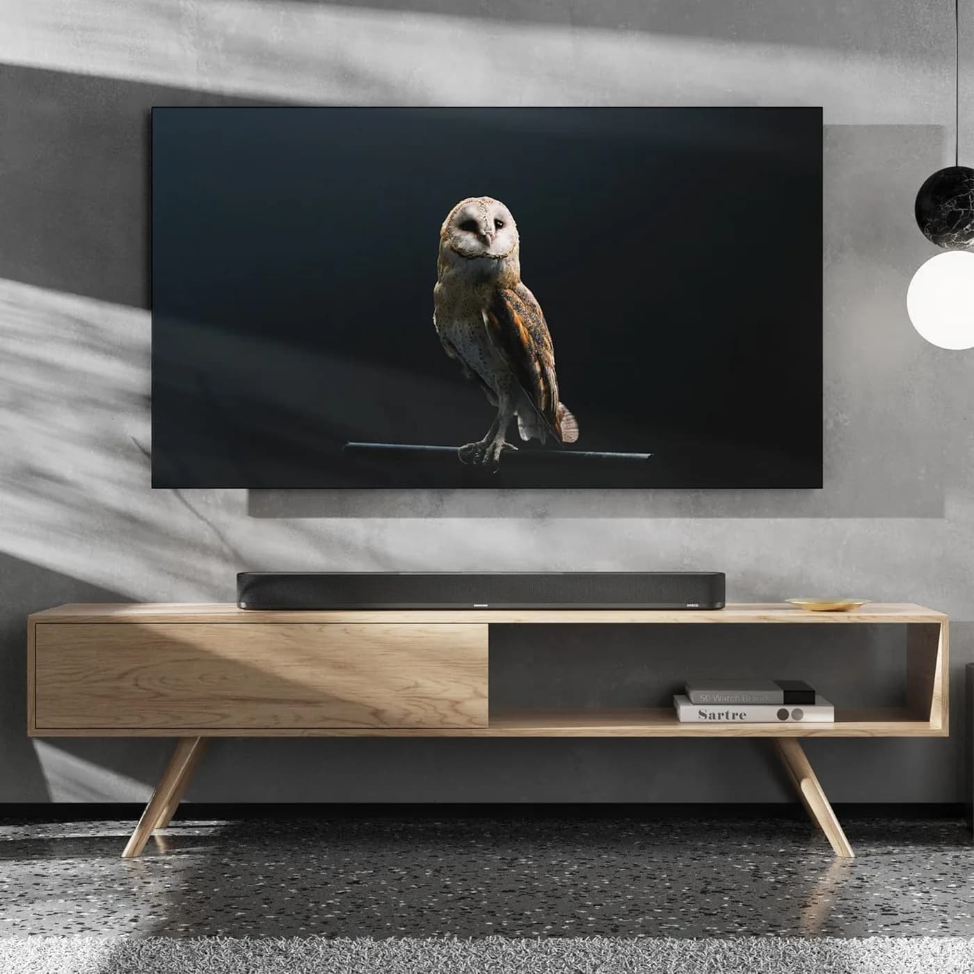 The AMBEO Soundbar Plus on a low wooden console beneath a wall-mounted television